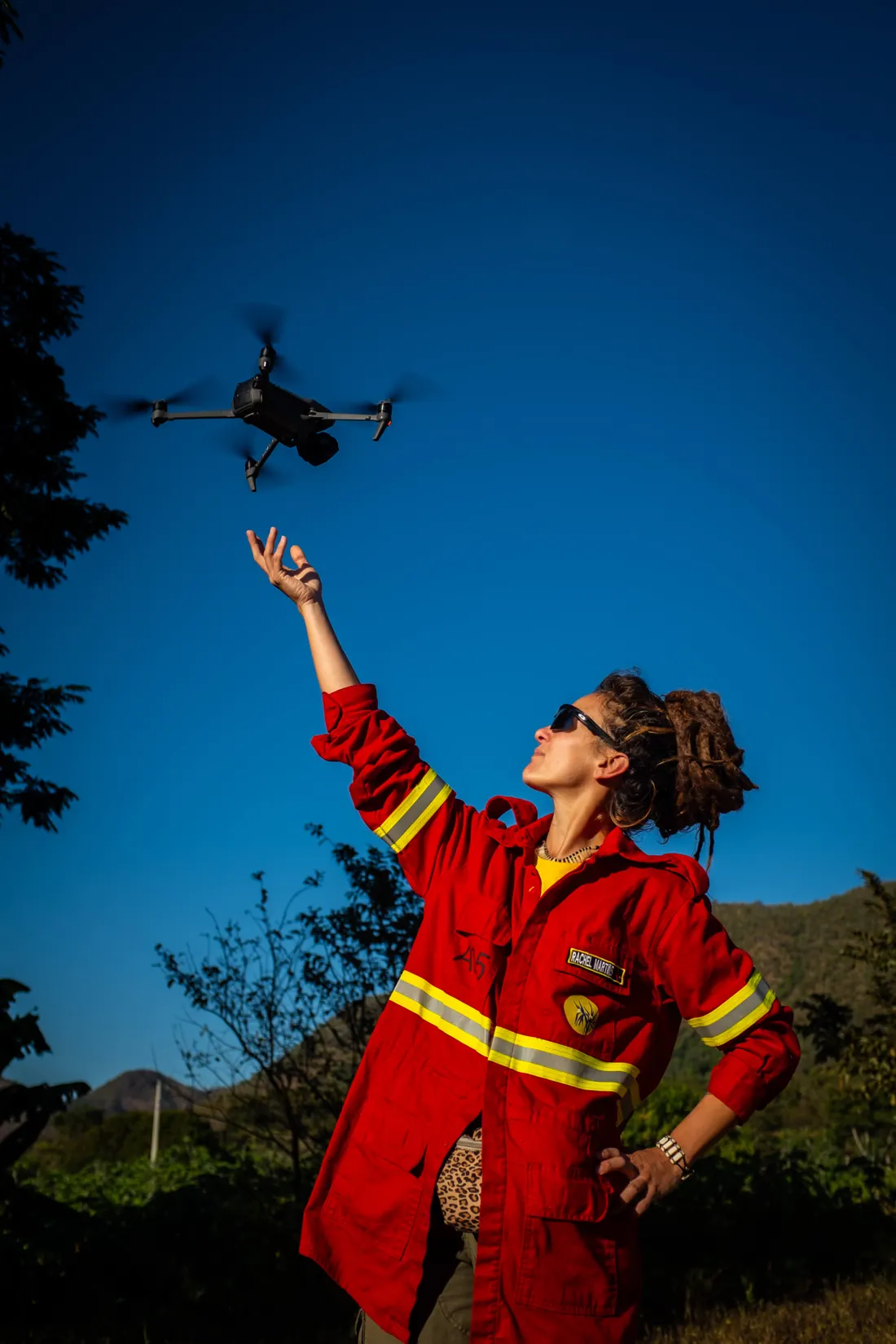 Brigadista de uniforme vermelho com faixas refletivas lança um drone ao céu azul